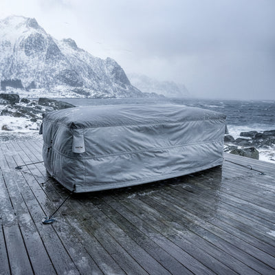Grey BAG’IN Nordic outdoor furniture cover protecting furniture on a deck in snow and strong wind by the coast.